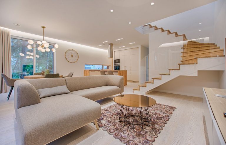 Phòng khách căn hộ mẫu với sofa màu be, bàn trà kính, cầu thang trắng và cửa kính lớn đón sáng
