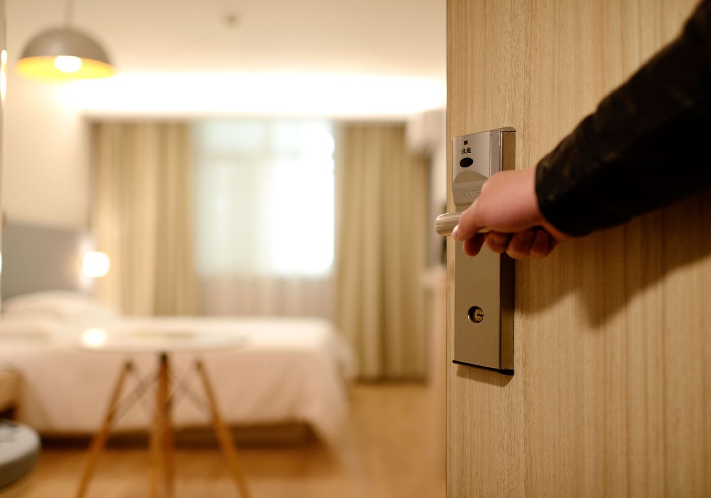 Bàn tay mở cửa phòng khách sạn bằng khoá thẻ, phía trong là phòng ngủ sáng đèn