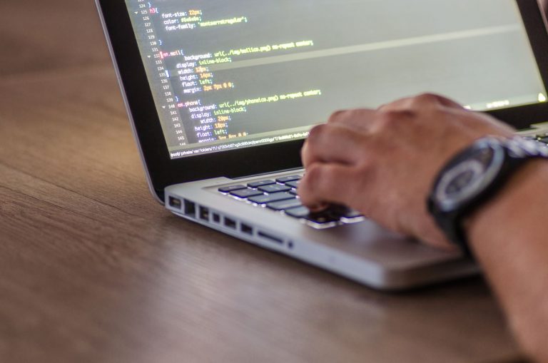 Bàn tay gõ phím laptop với mã nguồn hiển thị trên màn hình