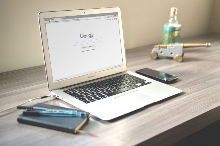 Bàn làm việc gỗ có laptop mở trang tìm kiếm, điện thoại và sổ tay